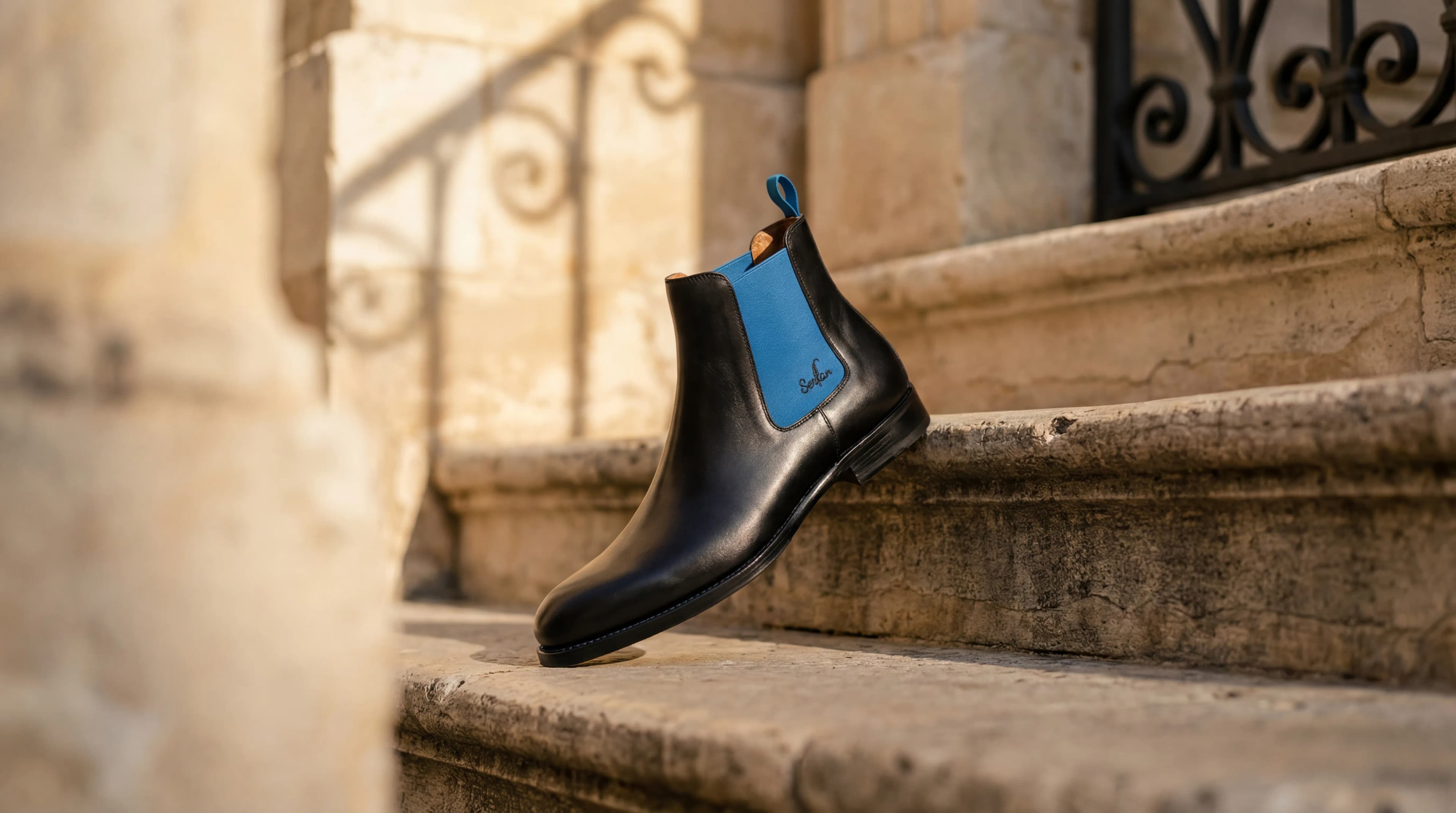 Serfan Chelsea Boots - Premium black leather with cobalt blue elastic accent on limestone steps
